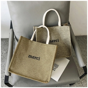 Detail shot of textured jute tote bags with black merci text on modern grey chair