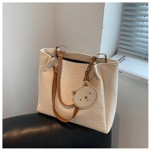 Close-up of beige embossed tote bag with brown straps and cute bear charm pendant