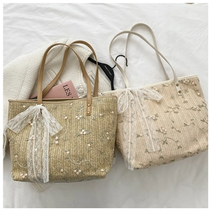 Detail of floral embroidery and large lace bow on a beige straw woven tote bag