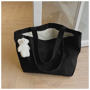 Detail of black corduroy tote bag with plush bear charm and zip closure on wood floor
