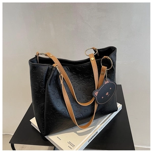 Detail of embossed cartoon patterns and teddy bear charm on black leather tote bag
