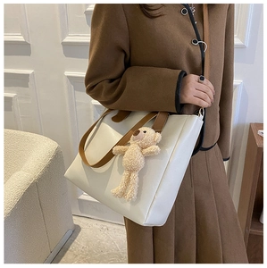 Detail of soft cream tote bag with dark brown straps and cute teddy bear charm pendant