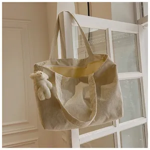 Detail of beige corduroy tote bag showing interior lining and plush bear charm