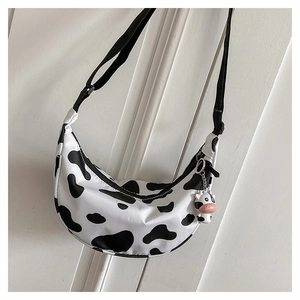 Detail of cow print nylon crescent bag featuring a cute cow plush charm and adjustable strap