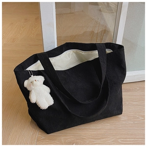 Detail of black corduroy tote bag with plush bear charm and sturdy shoulder straps