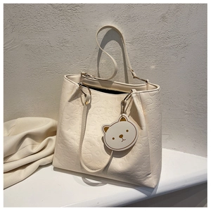 Detail view of cream tote bag featuring 3D cartoon embossing and cute bear charm