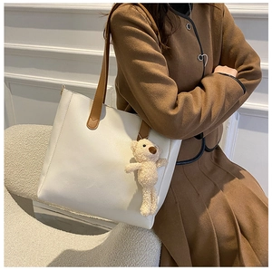 Detailed side view of cream leather tote bag with brown straps and plush bear charm
