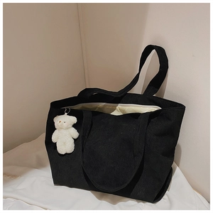 Detail of black corduroy tote bag featuring a zipper closure and plush bear pendant