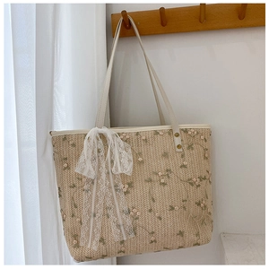 Detailed embroidery on woven straw tote bag with white lace bow and leather strap