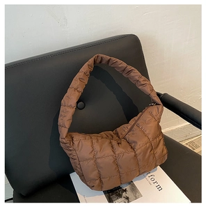 Detail of brown quilted nylon shoulder bag with soft padding on a leather chair