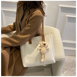 Detailed side view of white faux leather tote bag with brown straps and plush bear charm