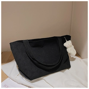 Detail of black corduroy tote bag showing vertical texture and white plush bear charm