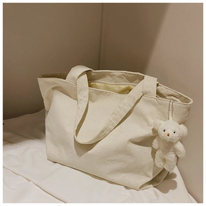 Detail of off-white corduroy tote bag featuring soft texture and plush bear charm decoration