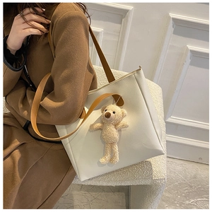 Detailed close-up of a cream faux leather tote bag featuring a cute plush bear pendant