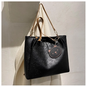 Detailed close-up of black embossed tote bag with cartoon patterns and cat head charm