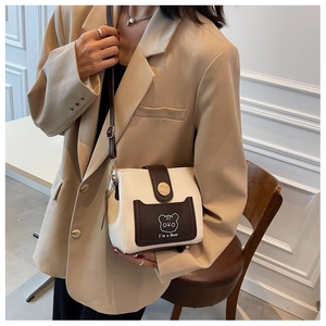 Detailed view of cream and brown crossbody bucket bag with cartoon bear on a model