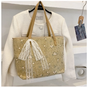 Detail of floral embroidery and white lace bow on a woven straw tote bag for women