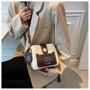 Detail of a beige and brown crossbody bucket bag with cartoon bear print and flower charm