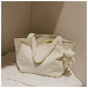 Detail of cream corduroy tote bag with plush bear charm and soft striped texture