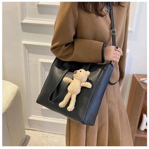 Fashionable black leather tote bag with a cute beige plush bear charm on a model