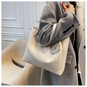 Detail of cream white tote bag with embossed cartoon patterns and cute bear charm