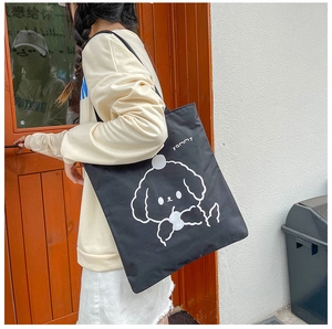 On-body shot of a black canvas tote bag featuring a cute white cartoon dog and yammy text