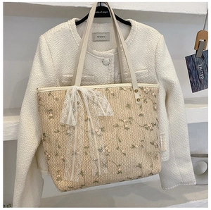 Detail of a beige woven tote bag with green floral embroidery and a white lace bow