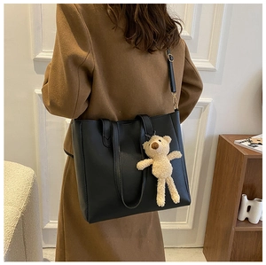 Close-up of black leather tote bag with a beige teddy bear charm on model shoulder