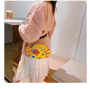 Détail du sac bandoulière jaune en forme de bonbon avec chaîne dorée porté par une fille