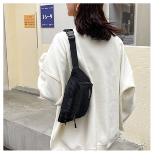 Detail view of black corduroy chest bag featuring fashion tag and adjustable strap buckle