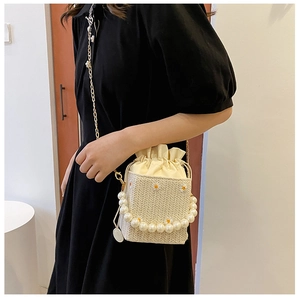Detail of straw bucket bag with daisy embroidery, pearl handle, and gold chain strap