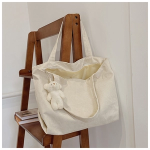 Detail of white corduroy tote bag texture with cute plush bear keychain on a wooden stand