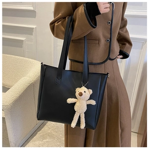 Black faux leather tote bag with teddy bear charm shown on a stylish shoulder carry