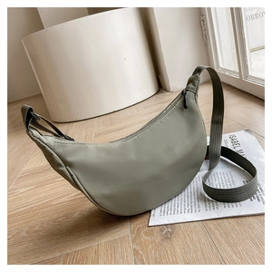 Sage green crescent nylon crossbody bag detail with wide shoulder strap on wooden floor