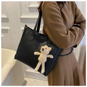 Detail of black PU leather tote bag with a cute beige plush bear charm and reinforced handles