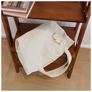 Close-up of cream corduroy tote bag with plush bear charm on a vintage wooden shelf