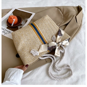 Close-up of woven straw bag with colorful stripes, silk scarf bow and cotton rope strap