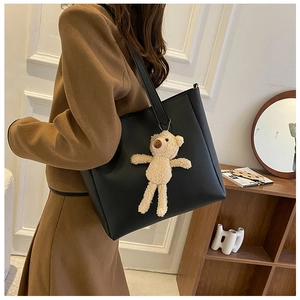 Detail of soft black leather tote bag featuring a cute beige teddy bear plush pendant