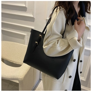 Detailed view of black faux leather tote bag with gold buckle on shoulder strap worn by model