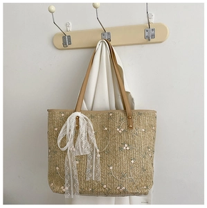 Detail of woven straw tote bag with floral embroidery and white lace ribbon decoration