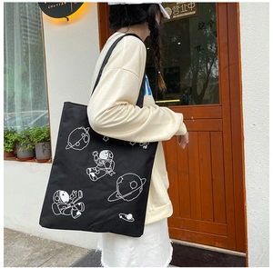 Detail of a black canvas tote bag featuring astronaut prints in a casual street style look