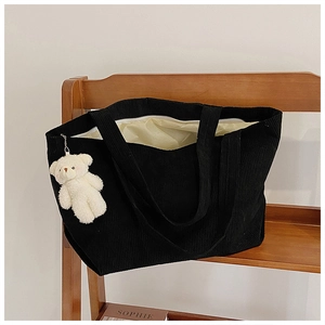 Detail of black corduroy tote bag texture and white teddy bear charm on wooden shelf