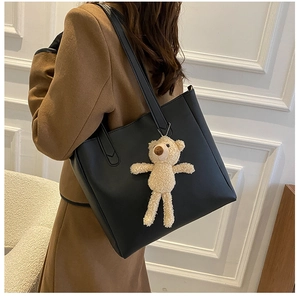Close-up of black soft leather tote bag featuring a cute beige plush bear pendant