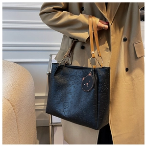Detail of black embossed tote bag with cartoon patterns, brown straps and cat pendant