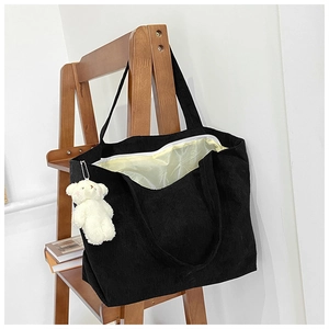 Close-up of black corduroy tote bag with white zipper and cute plush bear keychain