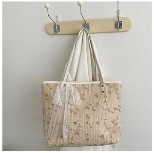 Detail of floral embroidery on a beige straw tote bag with white lace bow decoration