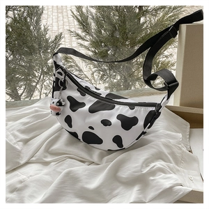 Detailed shot of cow print crescent bag with cute cow plush charm and nylon strap
