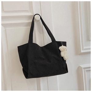 Detail of black corduroy tote bag featuring a white plush bear charm on white door