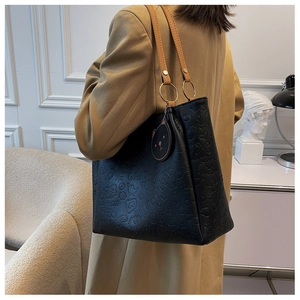 Detail of black embossed tote bag with cartoon patterns, brown straps and cat charm
