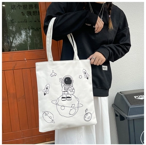 Outdoor shot of a white canvas tote bag with black astronaut prints and shoulder straps